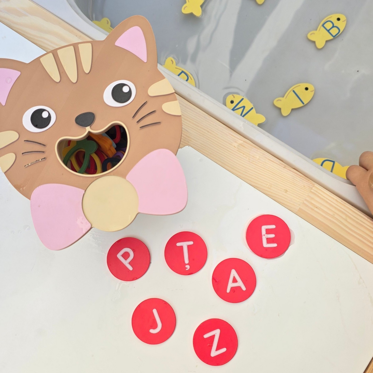 JoinIN educational set with 3D printed cat feeder, red magnetic letters, and yellow fish alphabet pieces in water.