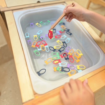 JoinIN rainbow fish sorting game with 70 colorful 3D printed fish and a wooden fishing tool in a water sensory bin
